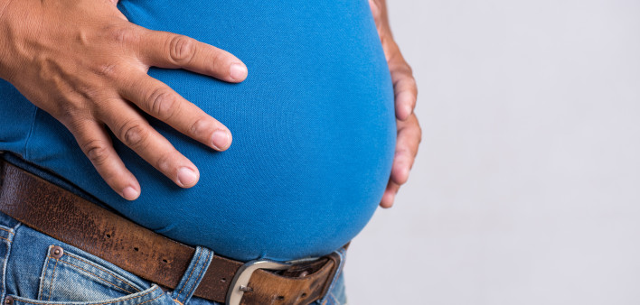 Overweight or fat adult man in very tight jeans on a gray background. Healthcare, medicine