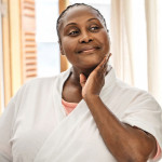 black woman looking at and touching her face in the mirror