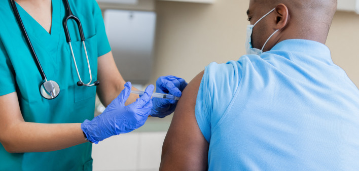 Nurse gives mature African American man a vaccination in doctor's office during coronavirus pandemic