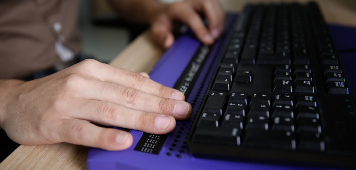 Blind person using computer with braille computer display and a computer keyboard.
