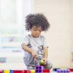 A cute little boy is sitting on the floor playing with building blocks at preschool.