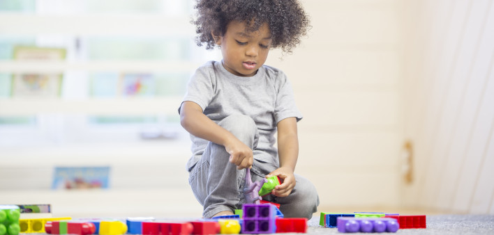 A cute little boy is sitting on the floor playing with building blocks at preschool.