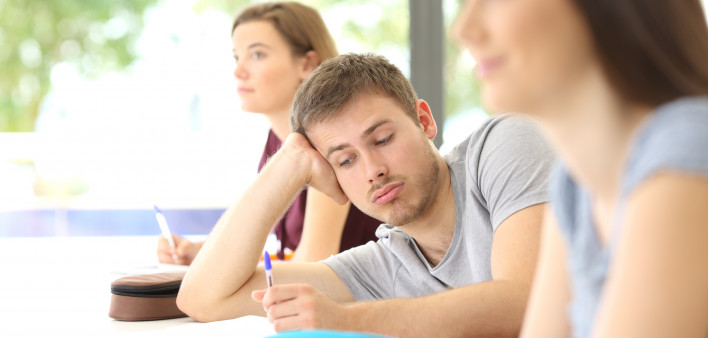 Bored student distracted during a class at classroom with classmates in the background