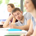 Bored student distracted during a class at classroom with classmates in the background