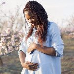 Portrait of a beautiful, young African woman enjoying her pregnancy at the orchard in bloom.