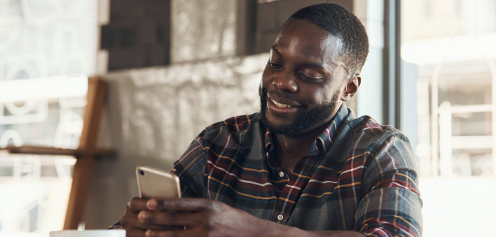 Shot of a handsome young man sitting and using his cellphone in a coffee shop during the day