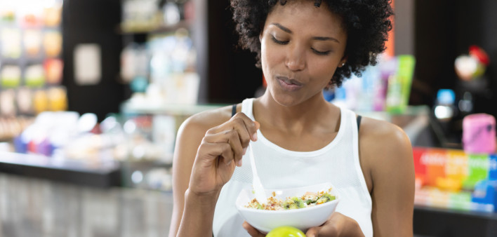 Beautiful black woman eating a healthy bowl and a green apple at the gym