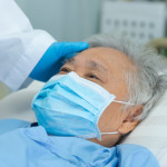 Doctor touching and checking Asian senior or elderly old lady woman patient wearing a face mask in hospital for protect infection and kill Novel Coronavirus Covid-19 virus