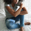 Lonely young latina woman sitting on bed. Depressed hispanic girl at home, looking away with sad expression.