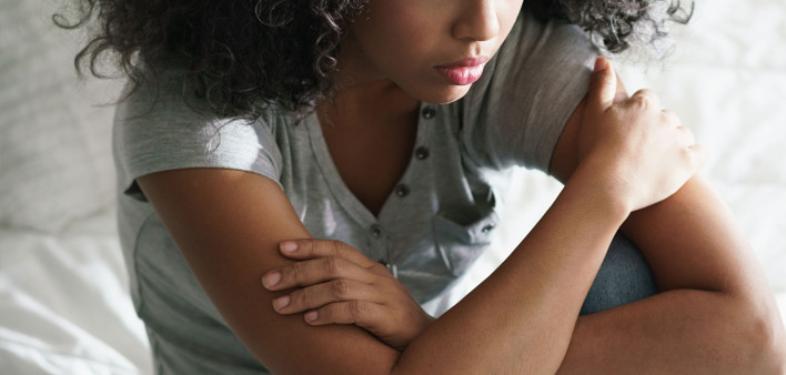 Lonely young latina woman sitting on bed. Depressed hispanic girl at home, looking away with sad expression.