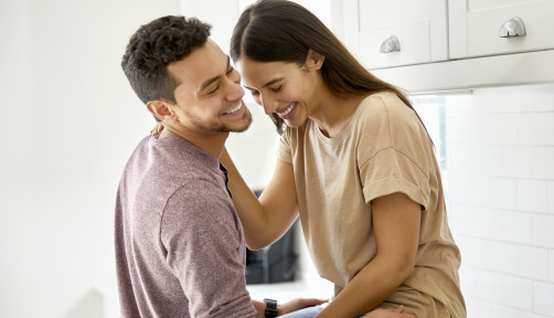 Cheerful Latino young couple talking in kitchen at home