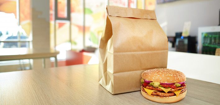 Cheeseburger and craft paper bag on wooden counter of cafe