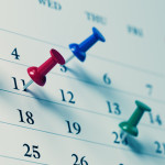 White calendar with colored push pins reminding important dates