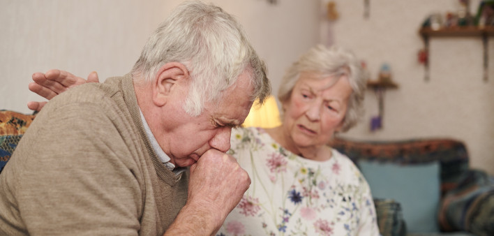 senior man with wife at home coughing badly