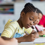 Cute pupil writing at desk in classroom