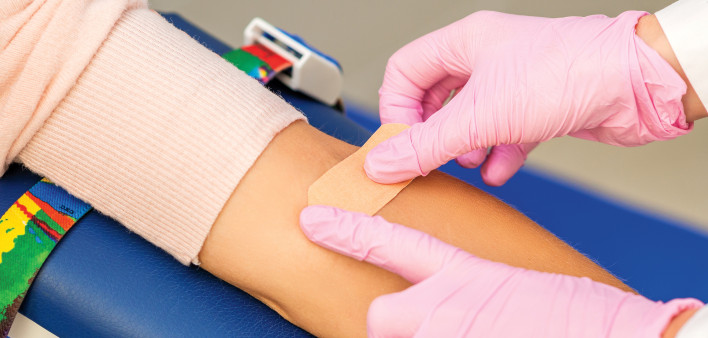 pink gloves putting band aid on arm after blood draw