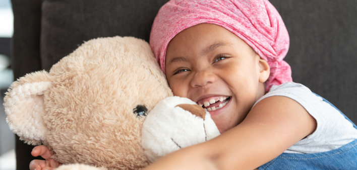 Happy girl with cancer hugs large teddy bear