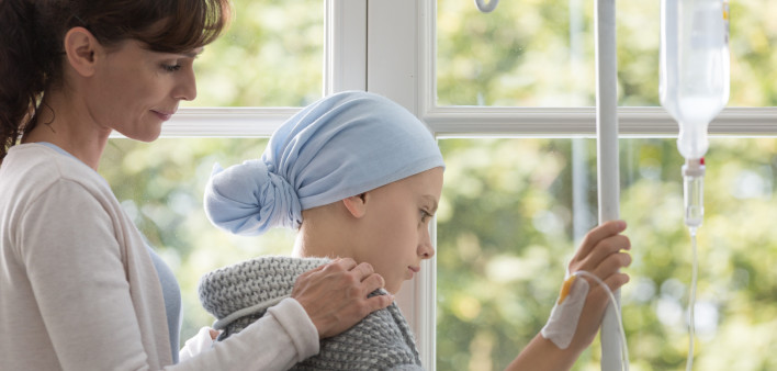 Caregiver hugging sick kid with headscarf holding drip in the hospital