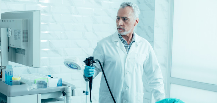 Serious mature doctor holding a modern endoscope and preparing for the procedure