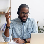 Smiling African American employee in headphones using laptop