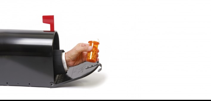 a hand holding a prescription coming out of a mailbox