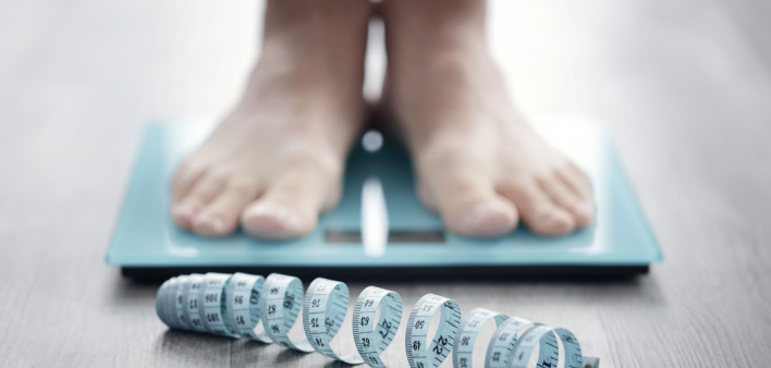mans feet on scale with measuring tape on floor