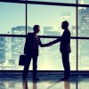  Businessmen shake hands in front of windows and skyline at night