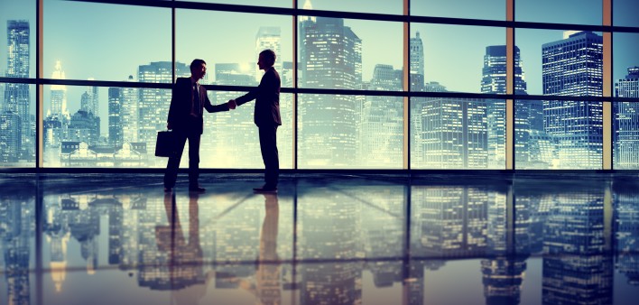  Businessmen shake hands in front of windows and skyline at night