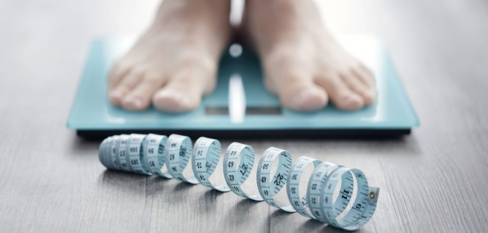 mans feet on scale with measuring tape on floor
