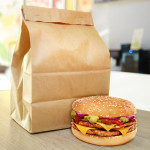 Cheeseburger and craft paper bag on wooden counter of cafe