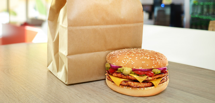 Cheeseburger and craft paper bag on wooden counter of cafe