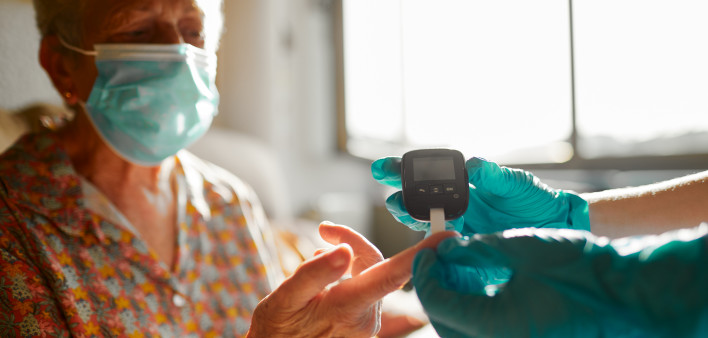 A nurse helping a senior woman perform a diabetes test