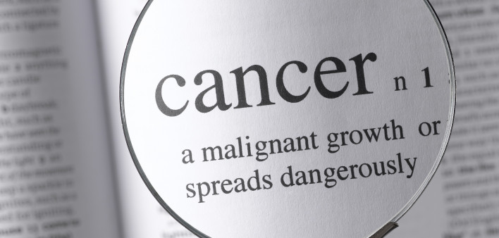 a magnifying glass magnifying the definition of cancer in a dictonary