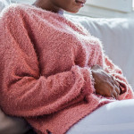 young black girl in pain, sitting on couch holding stomach