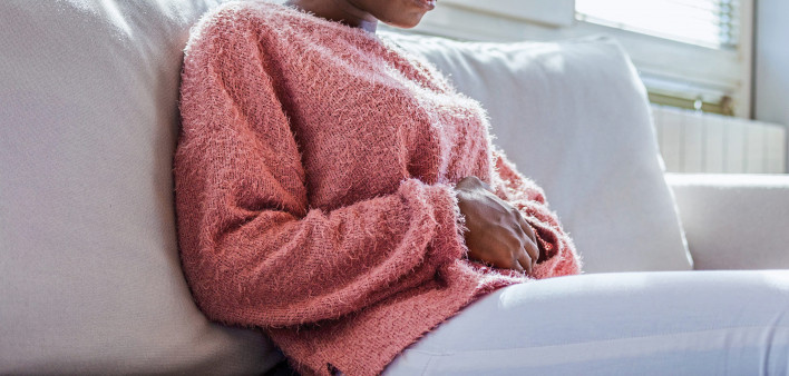 young black girl in pain, sitting on couch holding stomach
