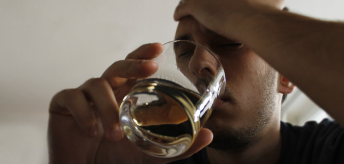 Drunk young adult male holding glass of alcohol, studio shot.