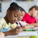 Cute pupil writing at desk in classroom