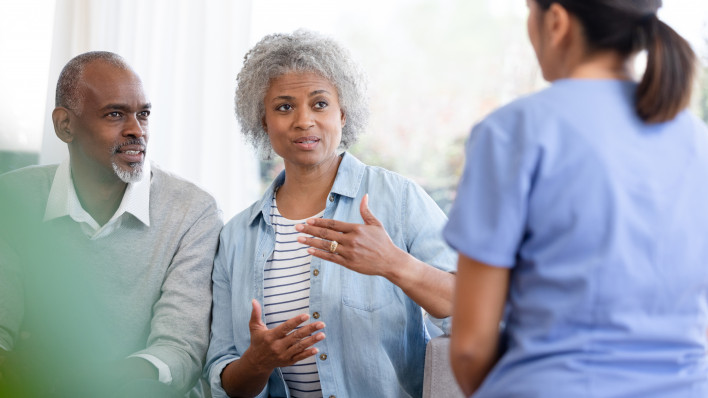 nurse sits in the living room and listens to senior couple.