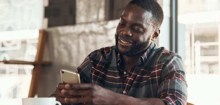 Shot of a handsome young man sitting and using his cellphone in a coffee shop during the day