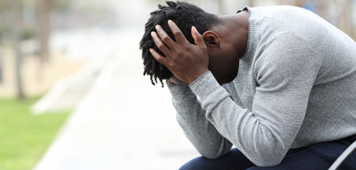 Side view portrait of a sad depressed black man sitting on a bench in a park