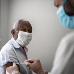 Nurse applying vaccine on patient's arm using face mask