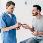 Patient sitting on couch and doctor writing prescription in massage cabinet at clinic