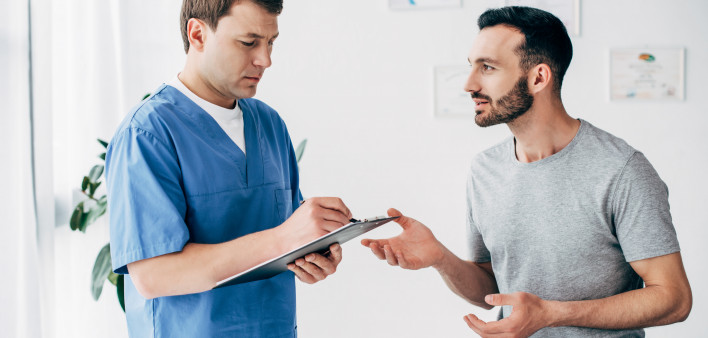 Patient sitting on couch and doctor writing prescription in massage cabinet at clinic