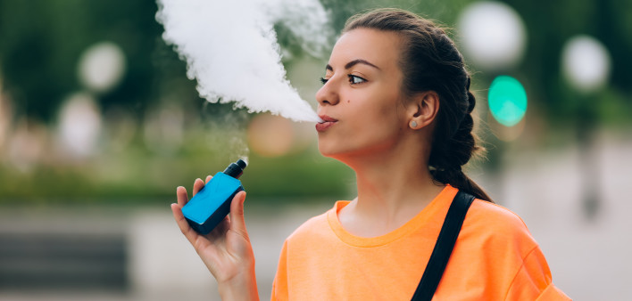 Pretty young hipster woman vape ecig, vaping device at the sunset.