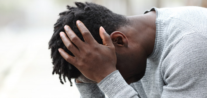 Side view portrait of a sad depressed black man sitting on a bench in a park