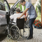 Helpful male nurse with senior lady on wheelchair helping her get in to the car