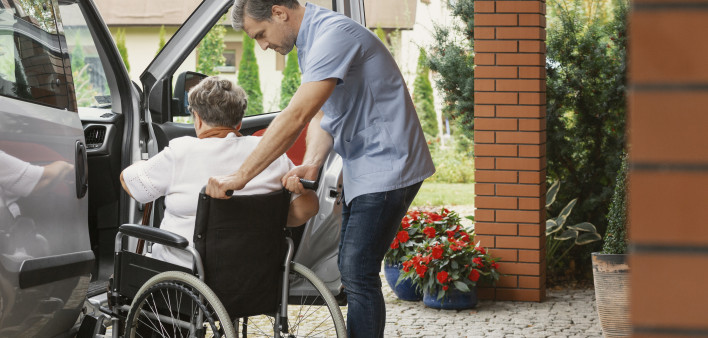 Helpful male nurse with senior lady on wheelchair helping her get in to the car