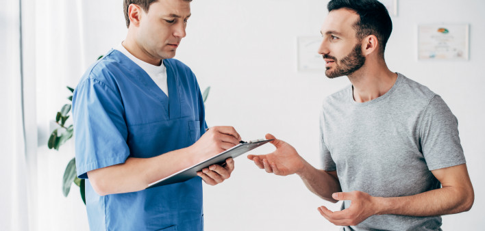 Patient sitting on couch and doctor writing prescription in massage cabinet at clinic