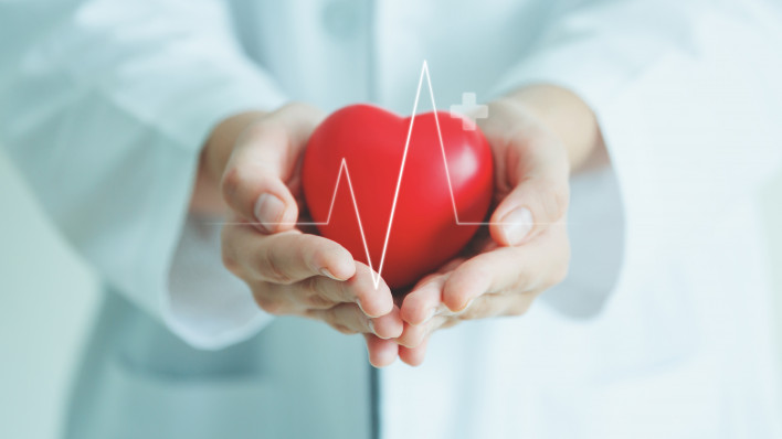 Female medical doctor holding red heart shape in hand with graphic of heart beat, cardiology and insurance concept