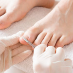 Pedicurist's hands in protective rubber gloves cutting toenails with scissors.